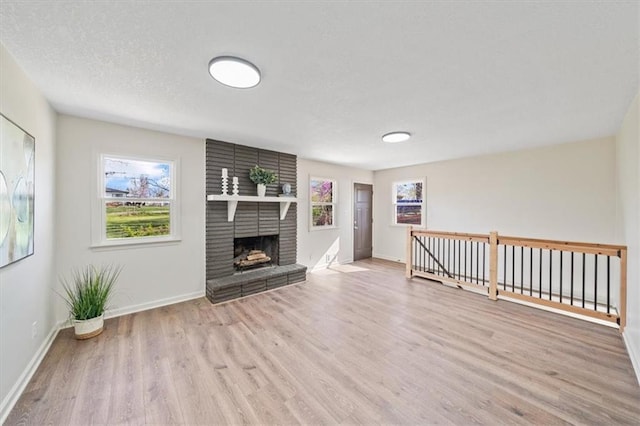 unfurnished living room with a brick fireplace, baseboards, a textured ceiling, and wood finished floors