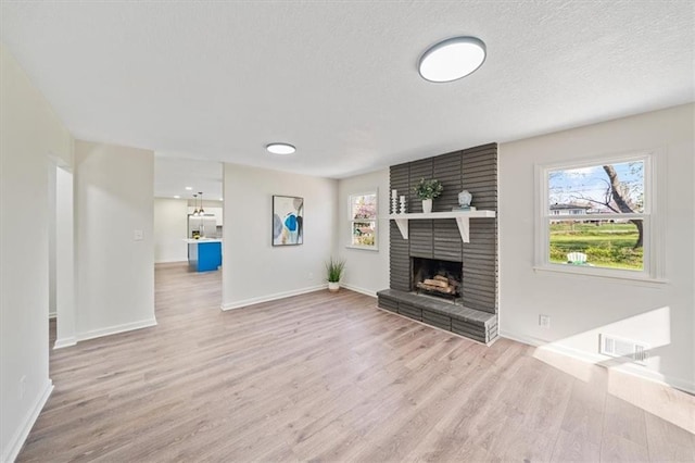 unfurnished living room with a textured ceiling, wood finished floors, a brick fireplace, and a healthy amount of sunlight