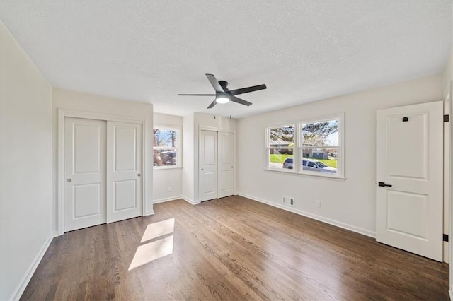 unfurnished bedroom featuring a textured ceiling, visible vents, wood finished floors, multiple closets, and baseboards