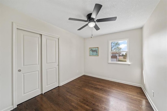 unfurnished bedroom featuring dark wood-type flooring, a textured ceiling, a closet, and baseboards