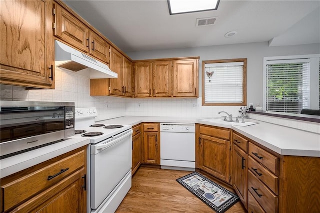 kitchen featuring a sink, white appliances, a peninsula, under cabinet range hood, and visible vents