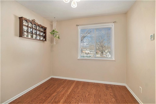 spare room with baseboards and wood finished floors
