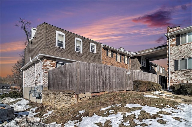 snow covered property featuring brick siding and fence