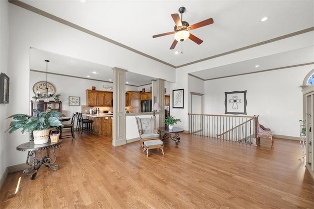 sitting room featuring baseboards, crown molding, light wood-style floors, ceiling fan, and decorative columns