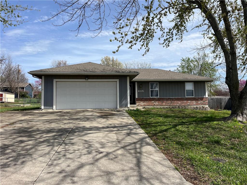 ranch-style home featuring driveway, a front yard, fence, an attached garage, and brick siding