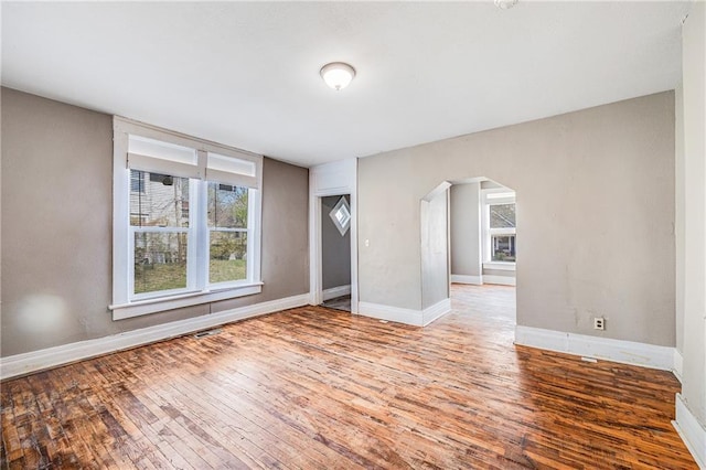 spare room with arched walkways, plenty of natural light, baseboards, and hardwood / wood-style floors