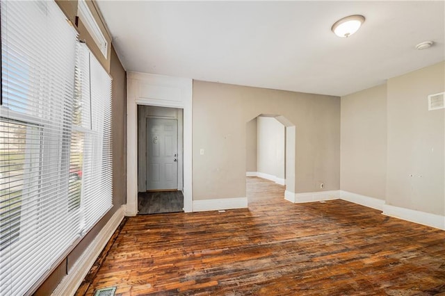 spare room featuring visible vents, baseboards, arched walkways, and wood finished floors