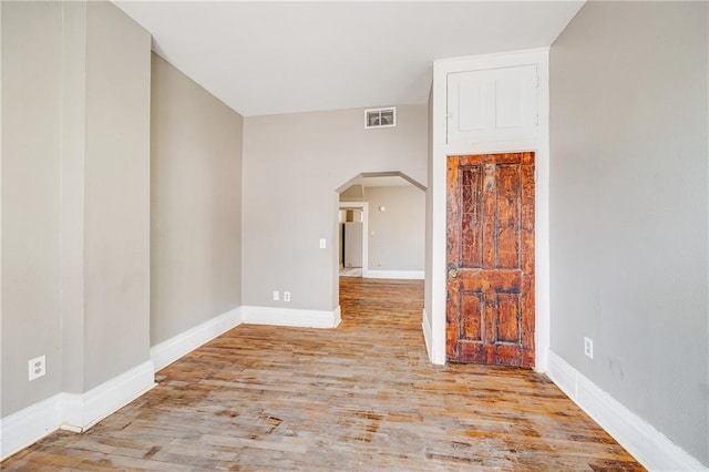 empty room featuring arched walkways, visible vents, baseboards, and wood finished floors