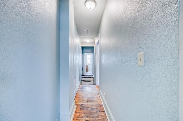 corridor featuring a textured wall, baseboards, attic access, and wood finished floors
