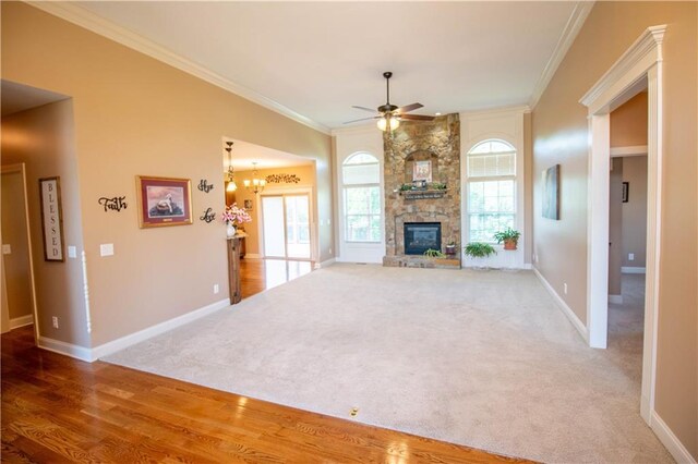 unfurnished living room featuring ceiling fan, ornamental molding, baseboards, a stone fireplace, and carpet flooring