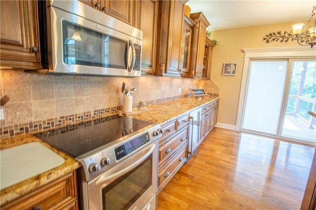 kitchen featuring appliances with stainless steel finishes, brown cabinets, decorative backsplash, and a chandelier