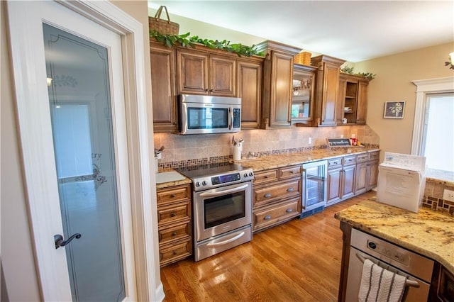 kitchen with appliances with stainless steel finishes, wine cooler, brown cabinetry, and backsplash