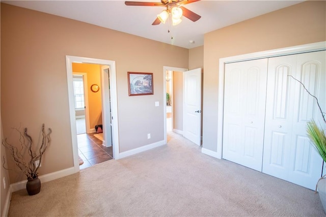 unfurnished bedroom featuring carpet, a closet, baseboards, a ceiling fan, and ensuite bath