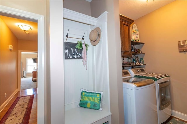 washroom featuring washing machine and clothes dryer, cabinet space, wood finished floors, and baseboards
