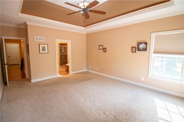 empty room with a tray ceiling, light colored carpet, ceiling fan, ornamental molding, and baseboards