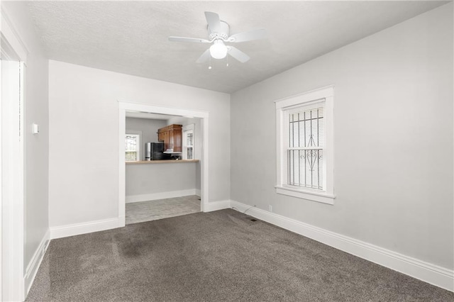 empty room featuring baseboards, a textured ceiling, a ceiling fan, and dark colored carpet
