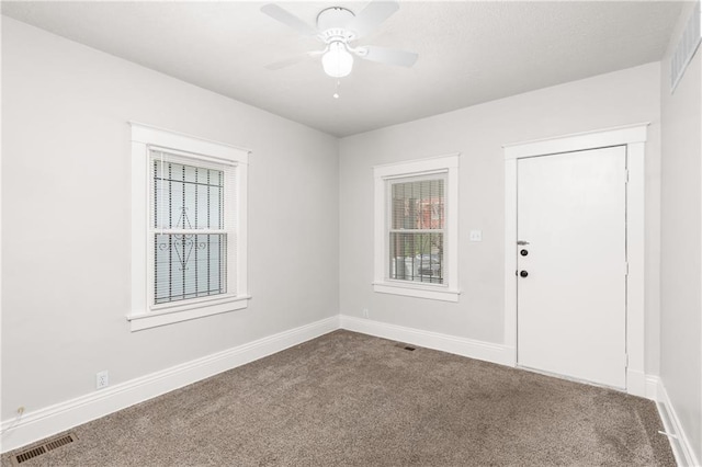 unfurnished room with baseboards, visible vents, dark colored carpet, and a ceiling fan