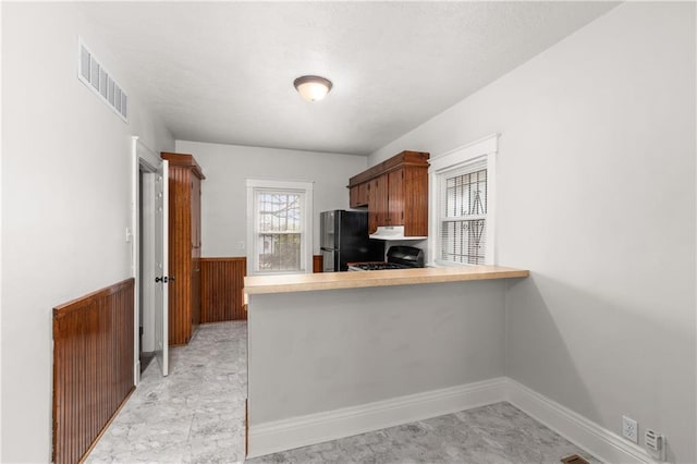 kitchen with light countertops, gas range, visible vents, freestanding refrigerator, and a peninsula