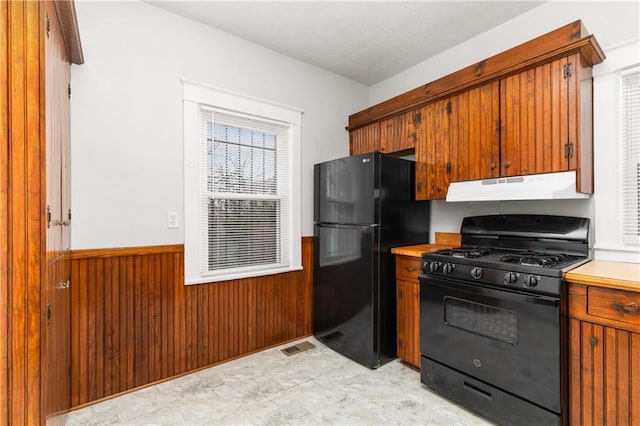 kitchen featuring visible vents, wood walls, under cabinet range hood, black appliances, and wainscoting