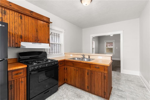 kitchen featuring light countertops, a sink, a peninsula, under cabinet range hood, and black appliances