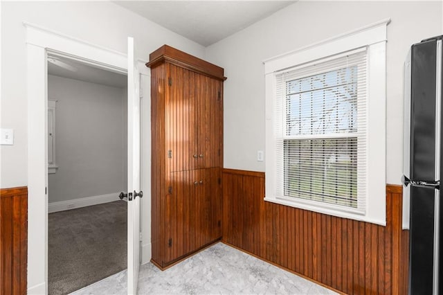 interior space with light carpet, wainscoting, wood walls, and freestanding refrigerator