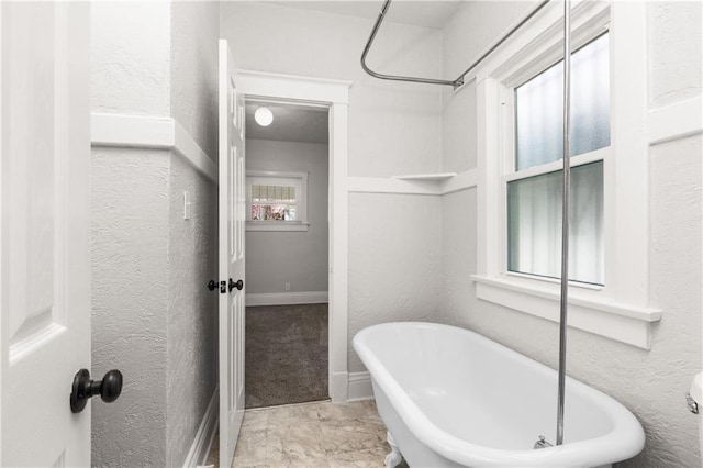 full bathroom featuring a soaking tub, baseboards, and a textured wall