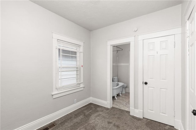 unfurnished bedroom featuring connected bathroom, baseboards, and dark carpet
