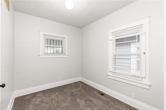 empty room with baseboards, visible vents, and dark carpet