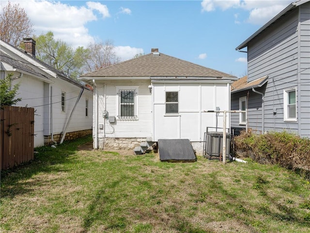 back of property with a shingled roof and a lawn