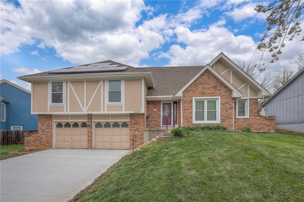 14638 W 85th Ter, Lenexa, KS 66215 - view of front of house with solar panels, an attached garage, brick siding, a front lawn, and driveway