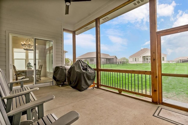 sunroom / solarium with a residential view, ceiling fan with notable chandelier, and visible vents