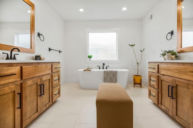 full bath featuring visible vents, baseboards, recessed lighting, two vanities, and a soaking tub