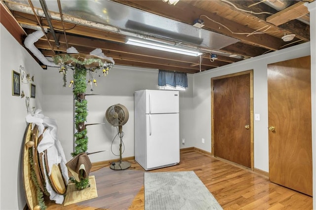 finished below grade area featuring freestanding refrigerator, light wood-style flooring, and baseboards