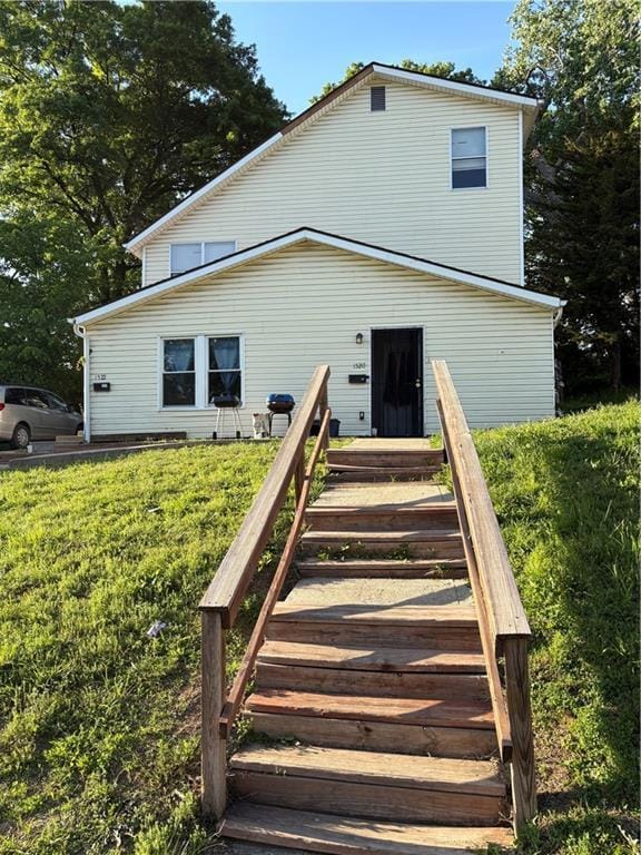 rear view of house featuring a lawn and stairway