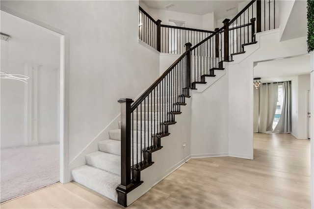 stairs featuring baseboards, wood finished floors, and a high ceiling