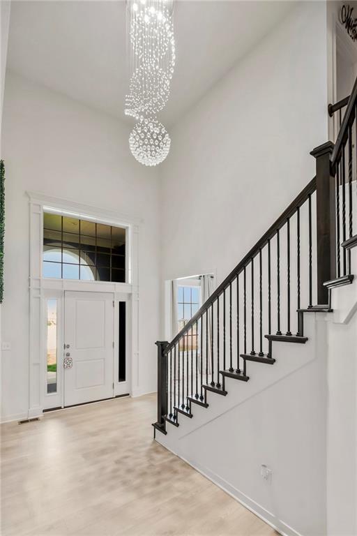 entrance foyer with baseboards, a towering ceiling, an inviting chandelier, wood finished floors, and stairs