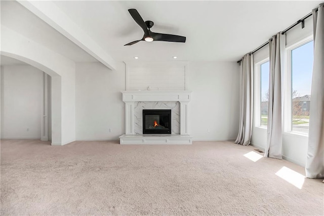 unfurnished living room with carpet flooring, arched walkways, baseboards, a ceiling fan, and a fireplace