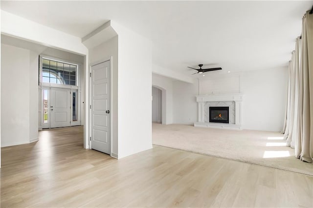 unfurnished living room featuring arched walkways, light wood-type flooring, a fireplace, and a ceiling fan