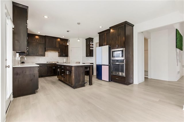 kitchen with light wood finished floors, dark brown cabinetry, decorative backsplash, light countertops, and appliances with stainless steel finishes