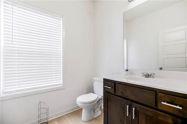bathroom with baseboards, wood finished floors, vanity, and toilet