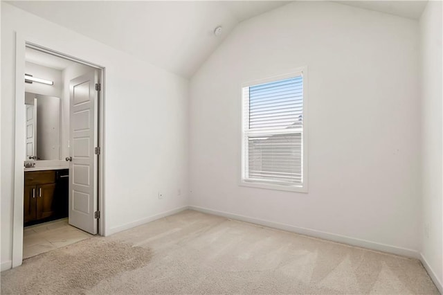 unfurnished bedroom with light colored carpet, baseboards, lofted ceiling, and ensuite bathroom