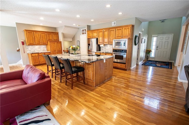 kitchen featuring stainless steel appliances, brown cabinetry, light wood-style floors, a textured ceiling, and recessed lighting
