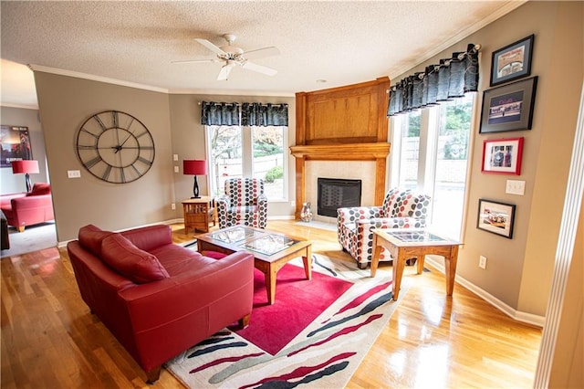living room featuring a textured ceiling, a fireplace, light wood-style flooring, ornamental molding, and baseboards