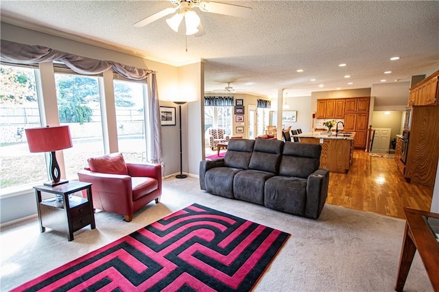 living area with ceiling fan, light carpet, a textured ceiling, recessed lighting, and crown molding