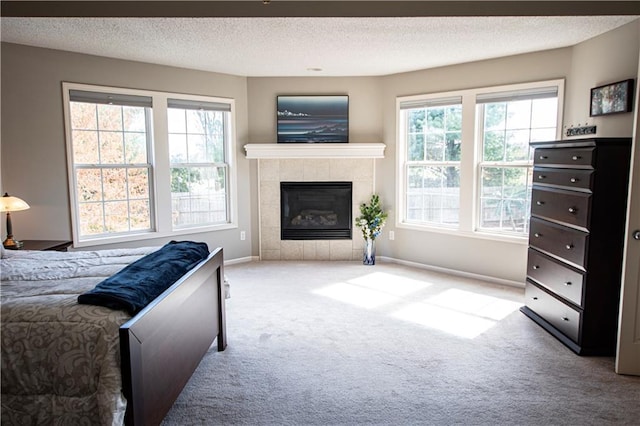 carpeted bedroom featuring multiple windows, a textured ceiling, baseboards, and a tile fireplace