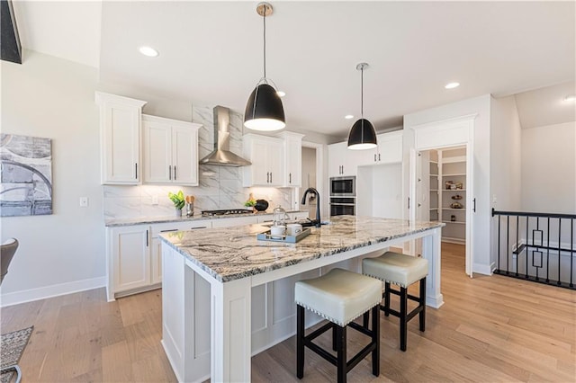 kitchen with wall chimney exhaust hood, light wood-type flooring, white cabinets, backsplash, and recessed lighting
