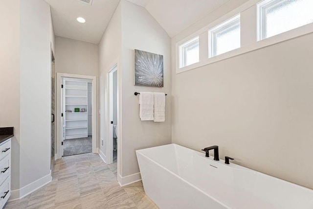 full bath featuring vanity, marble finish flooring, baseboards, a soaking tub, and lofted ceiling