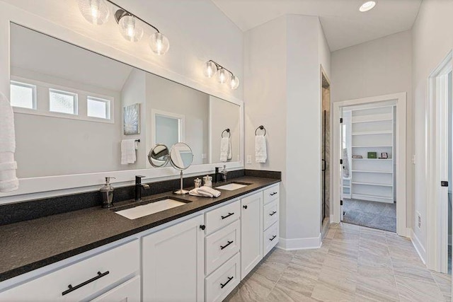 bathroom with double vanity, a shower stall, a spacious closet, and baseboards