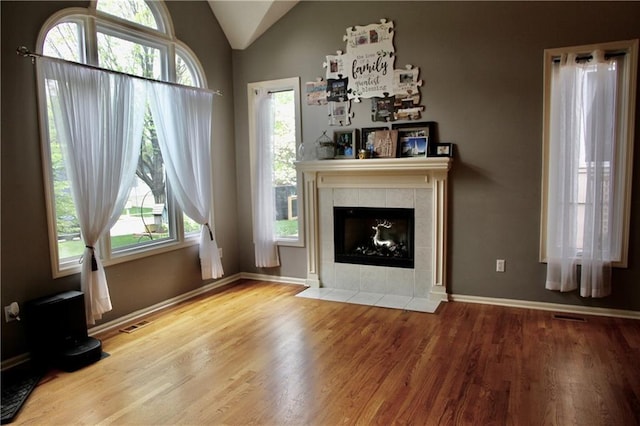 living area featuring vaulted ceiling, a tile fireplace, wood finished floors, and a wealth of natural light