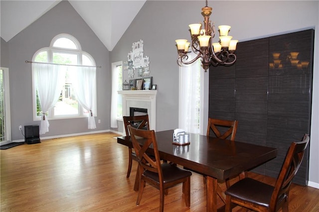 dining room with lofted ceiling, wood finished floors, a fireplace, baseboards, and a chandelier